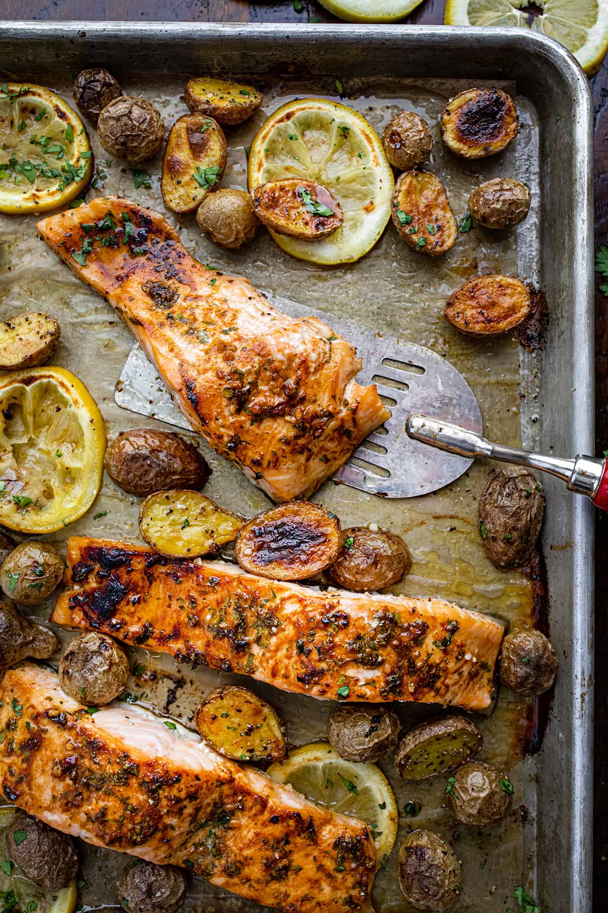 Picking up a Piece of Salmon from a Sheet Pan with Lemons and Potatoes.