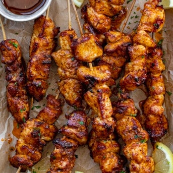 Lemon Pepper Chicken Skewers From Overhead With Sauce on a Brown Parchment Paper with Lemons.