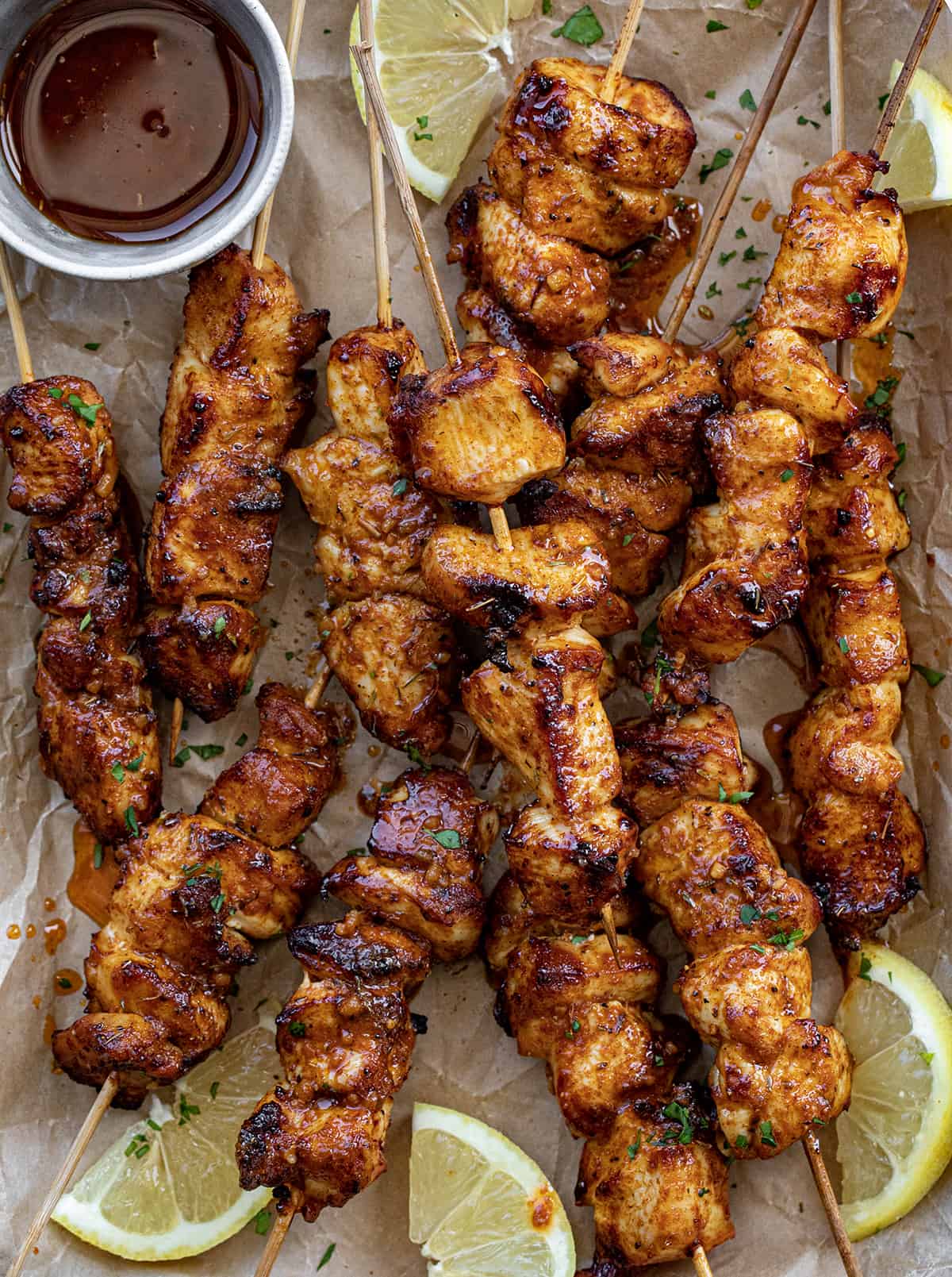 Lemon Pepper Chicken Skewers From Overhead With Sauce on a Brown Parchment Paper with Lemons.