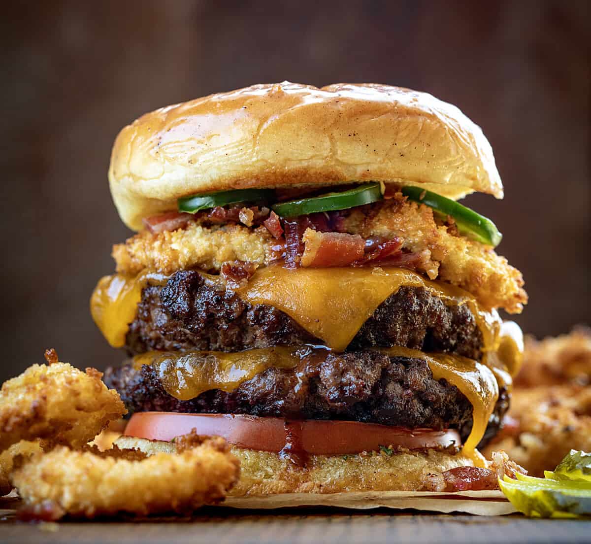 Close up of a Rodeo Burger on a Cutting Board Surrounded by Onion Rings.