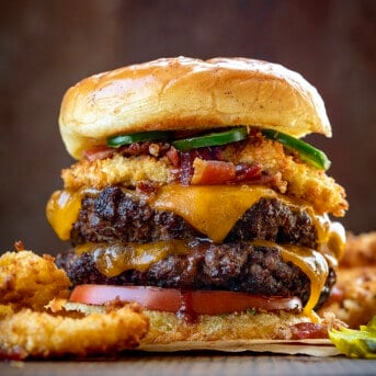 Close up of a Rodeo Burger on a Cutting Board Surrounded by Onion Rings.