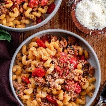 Bowls of Tomato Basil Pasta with Italian Sausage on Cutting Board with Fresh Parmesan and Basil.