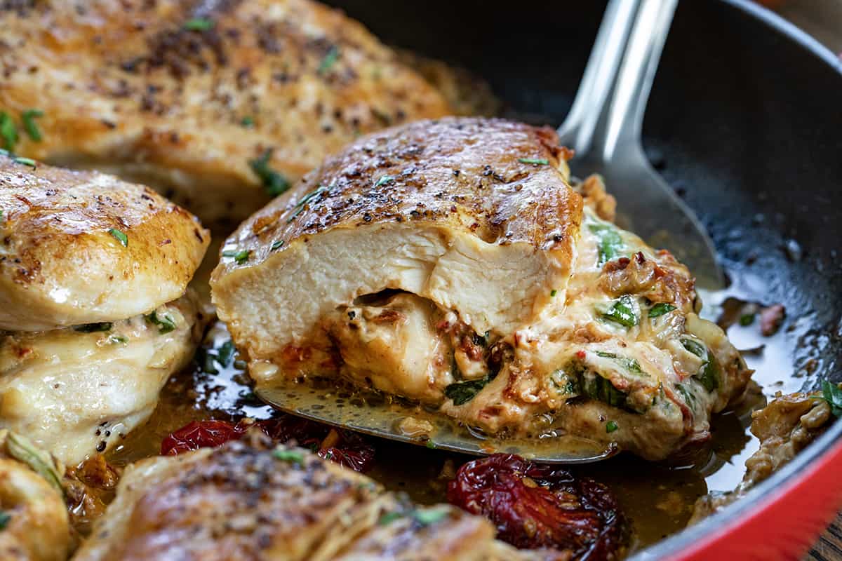 Spatula Picking up Cut in Half Stuffed Sun-Dried Tomato Chicken.