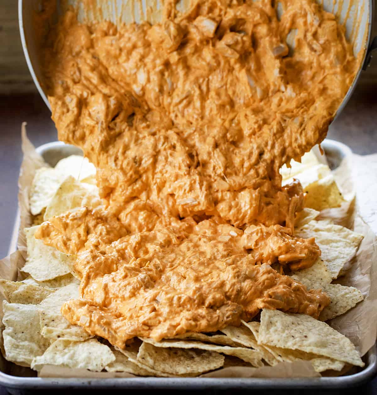 Pouring Buffalo Chicken Mixture Over Chips to Make Buffalo Chicken Nachos.