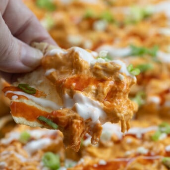 Hand Holding a Chip with Buffalo Chicken Toppings on it.
