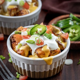 Bowls of Cheesy Fiesta Potatoes on a Dark Cutting Board with Jalapeno and Forks.