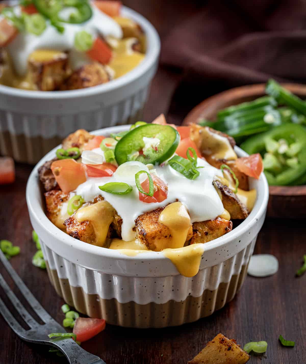 Bowls of Cheesy Fiesta Potatoes on a Dark Cutting Board with Jalapeno and Forks. 