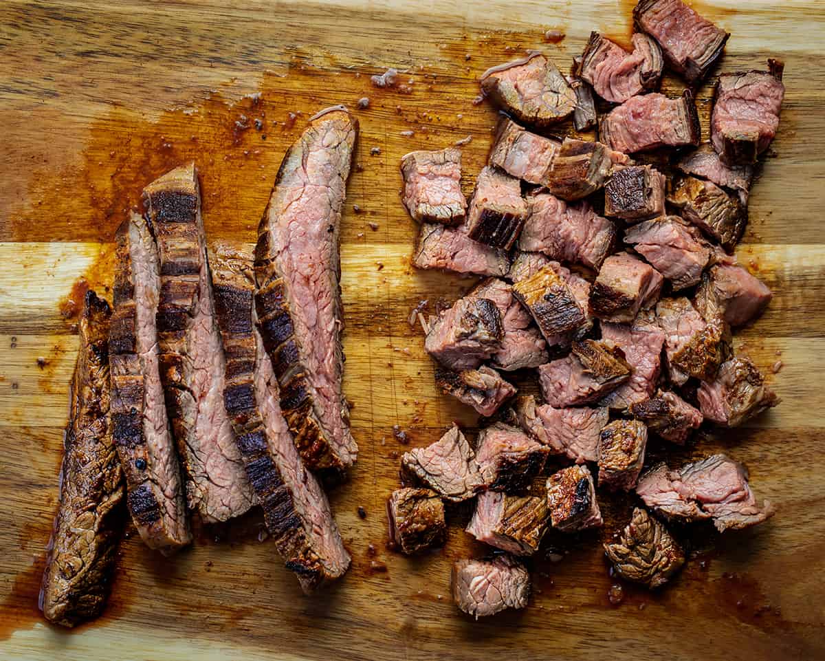 A Flank Steak on a Cutting Board with Some Pieces Cut into Strips and Others Cut into Cubes to Make Chipotle Steak.