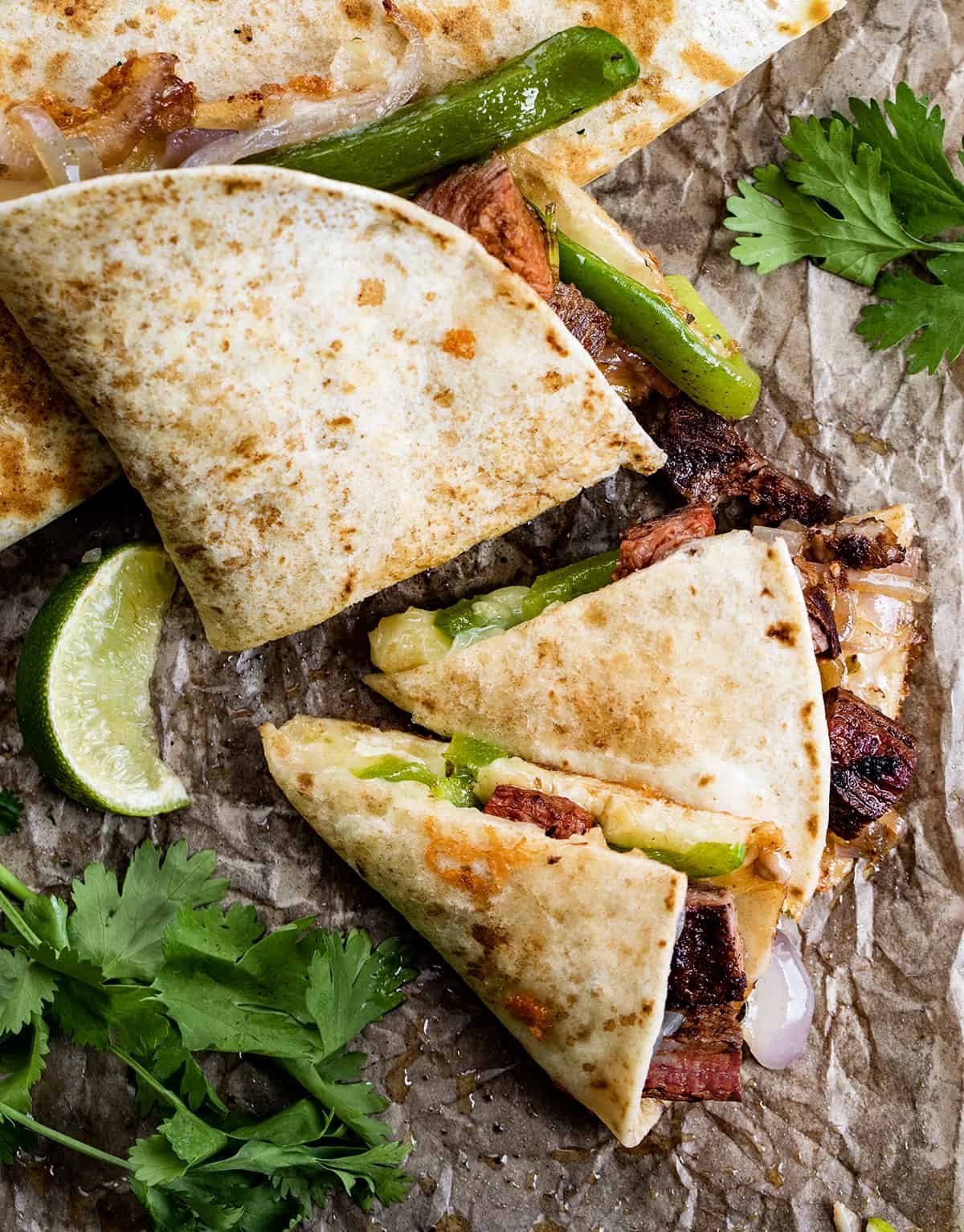 Cut up Chipotle Steak Quesadilla on a Piece of Parchment Paper with Cilantro and Lime.