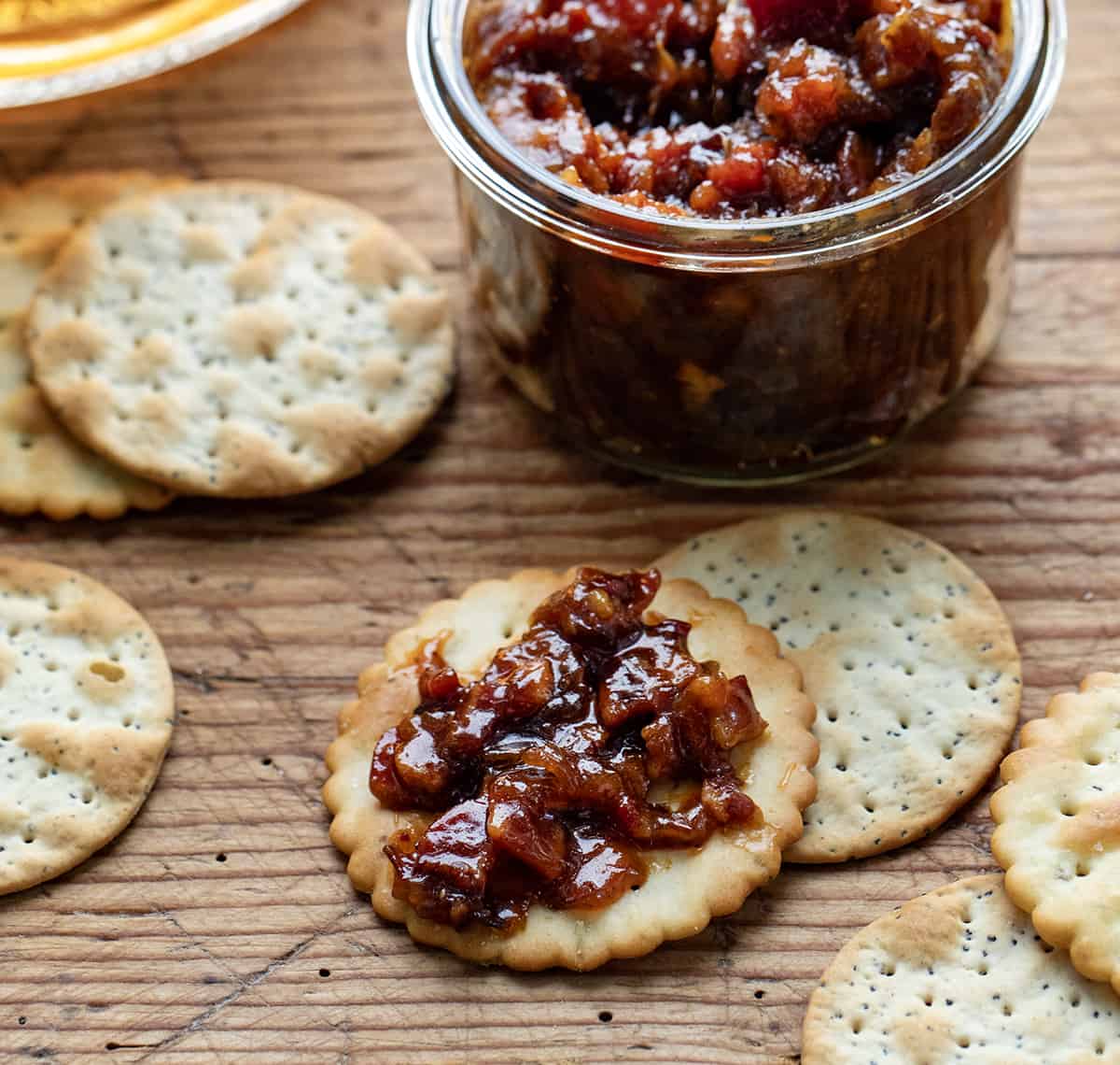 Cracker with Whiskey Bacon Jam on it Next to a Jar of Whiskey Bacon Jam.