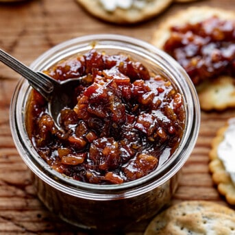 Jar of Whiskey Bacon Jam with a Spoon and Surrounded by Crackers.