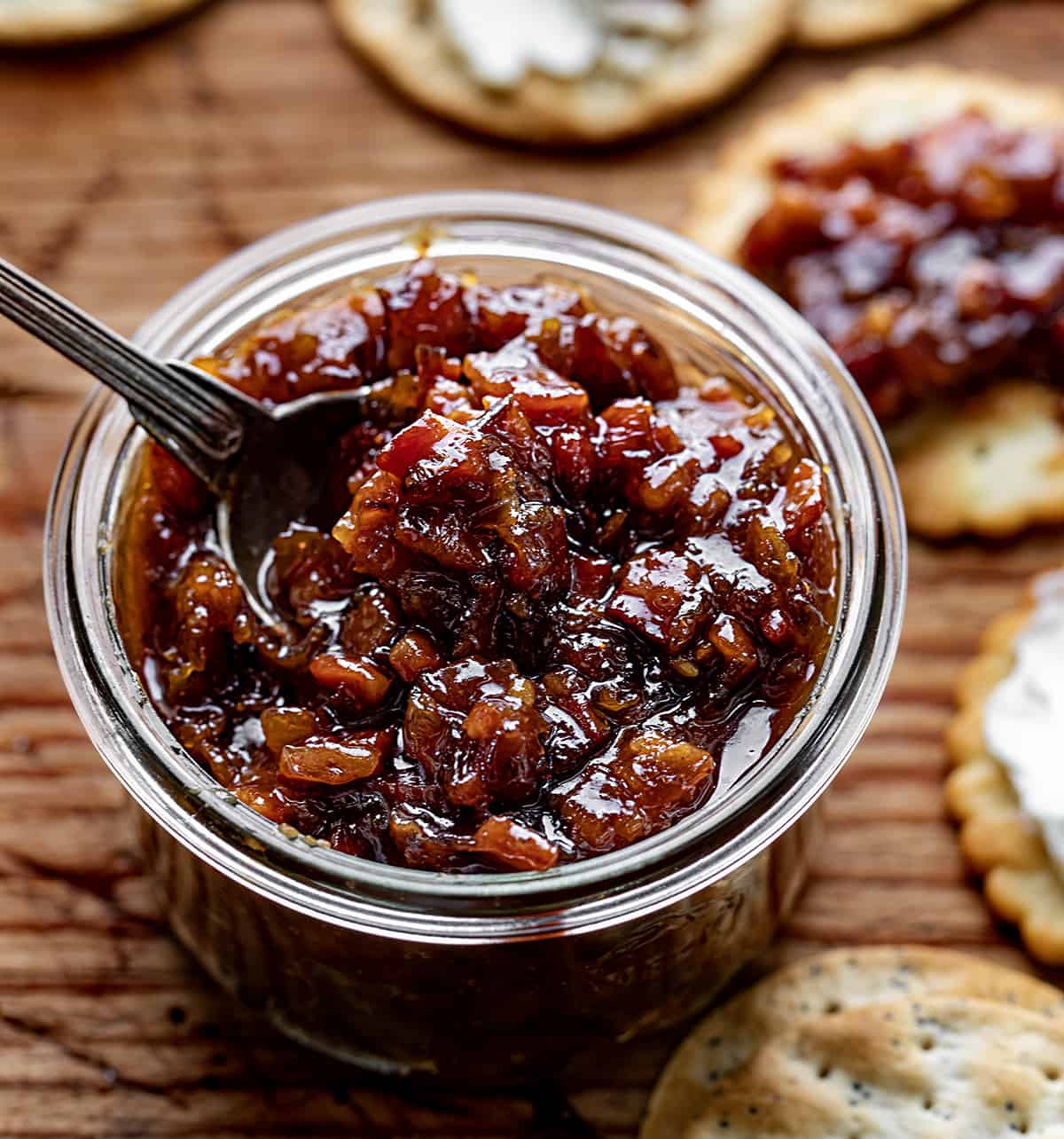 Jar of Whiskey Bacon Jam with a Spoon and Surrounded by Crackers.