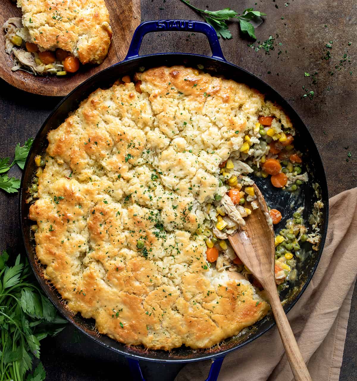 Skillet of Butter Swim Biscuit Chicken Pot Pie with Some Removed and a Wooden Spoon.