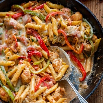 Skillet of Chicken Fajita Pasta with a Spoon in it on a Wooden Table.