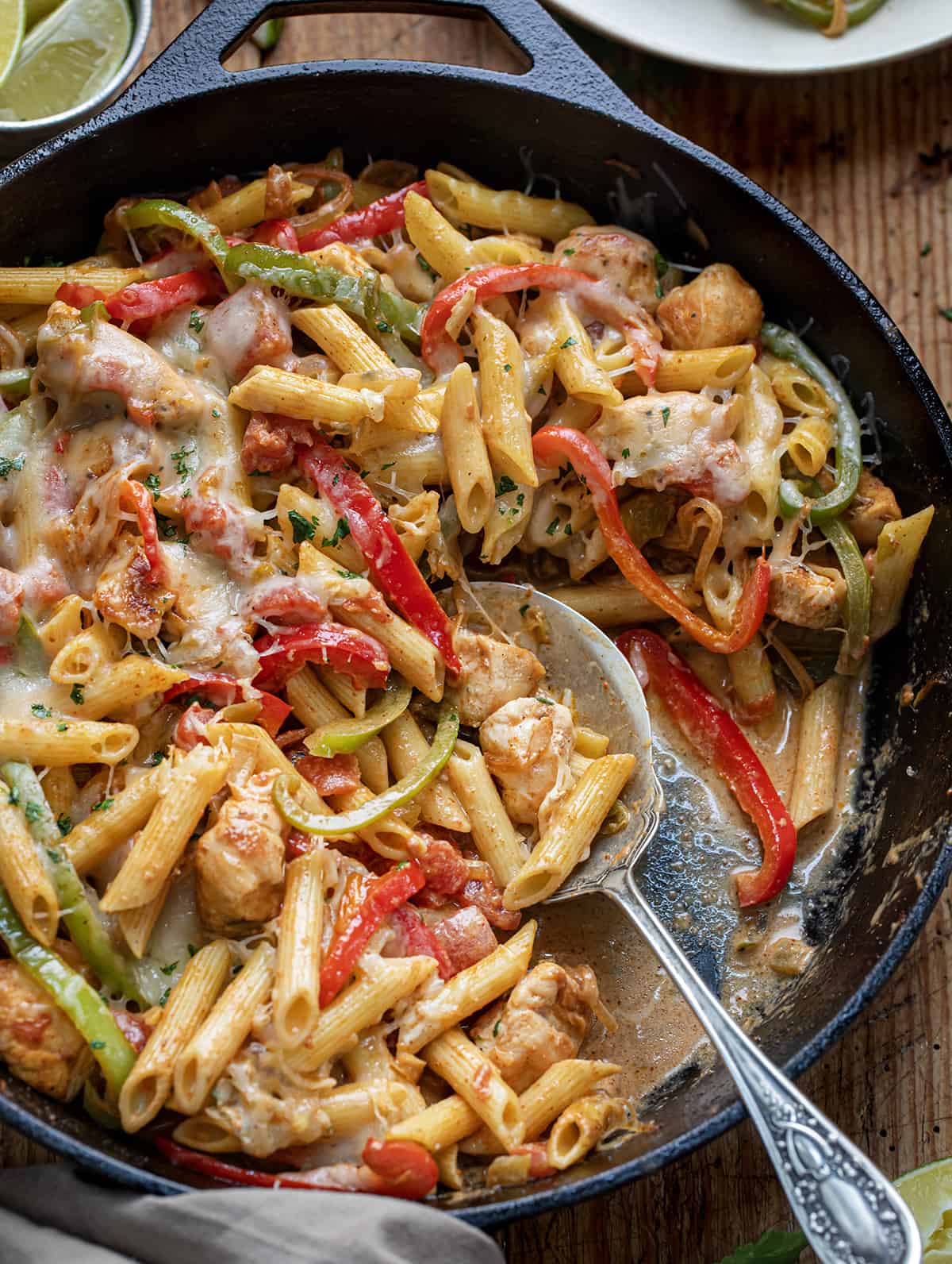 Skillet of Chicken Fajita Pasta with a Spoon in it on a Wooden Table. 