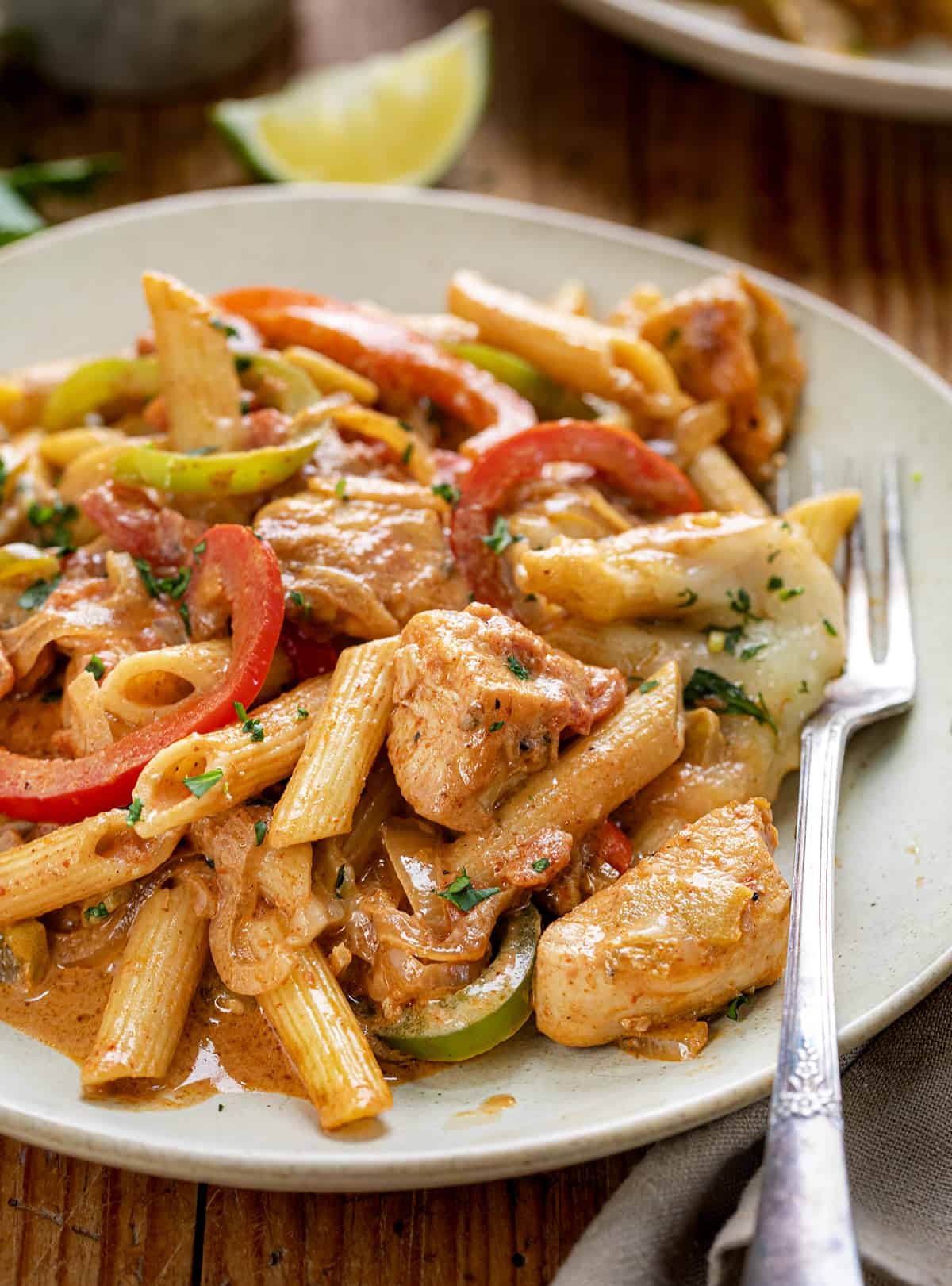 Close up of a Plate of Chicken Fajita Pasta with Limes in the Background.