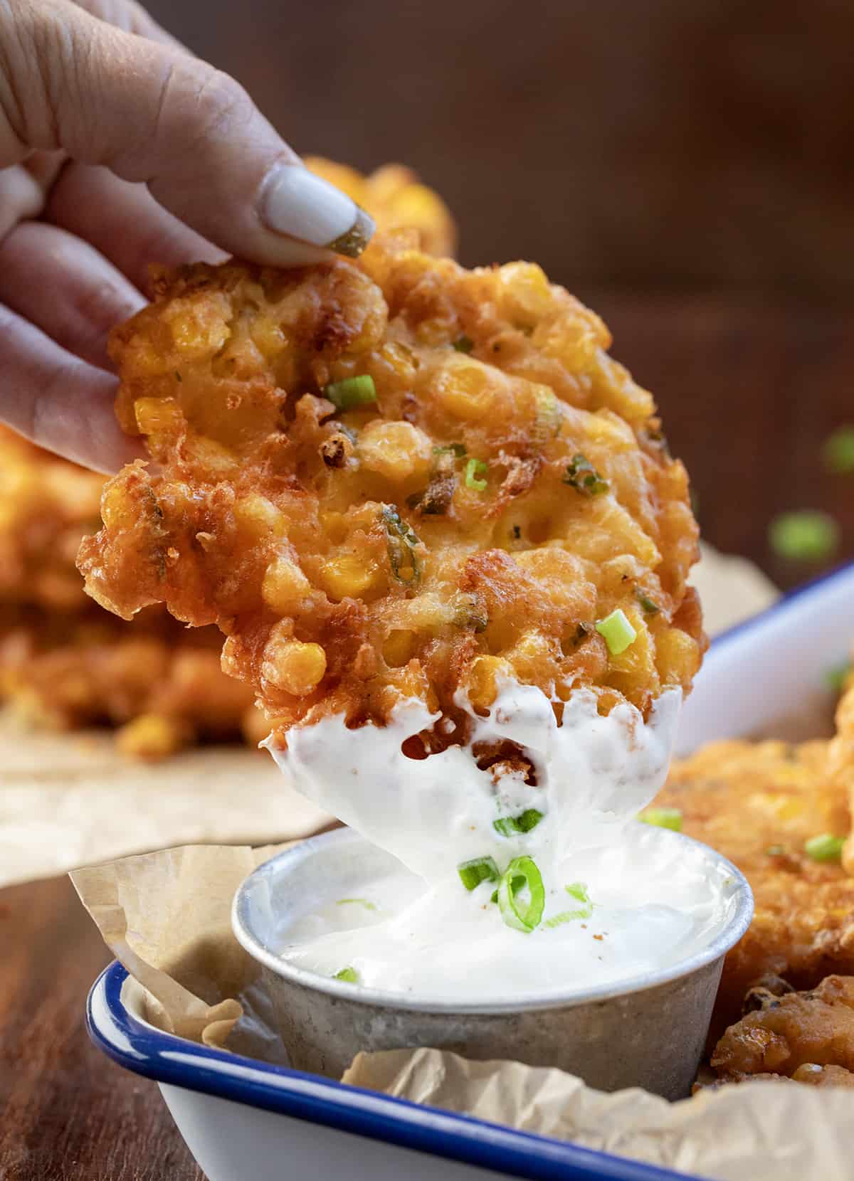 Hand Dipping Corn Fritter into Sour Cream Sauce.