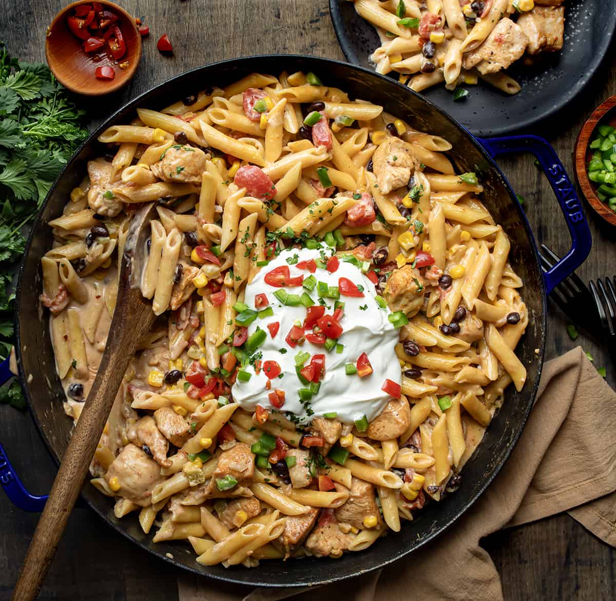 Skillet of Southwest Chicken Pasta with a Wooden Spoon and Some on a Plate Next to the Skillet from Overhead.