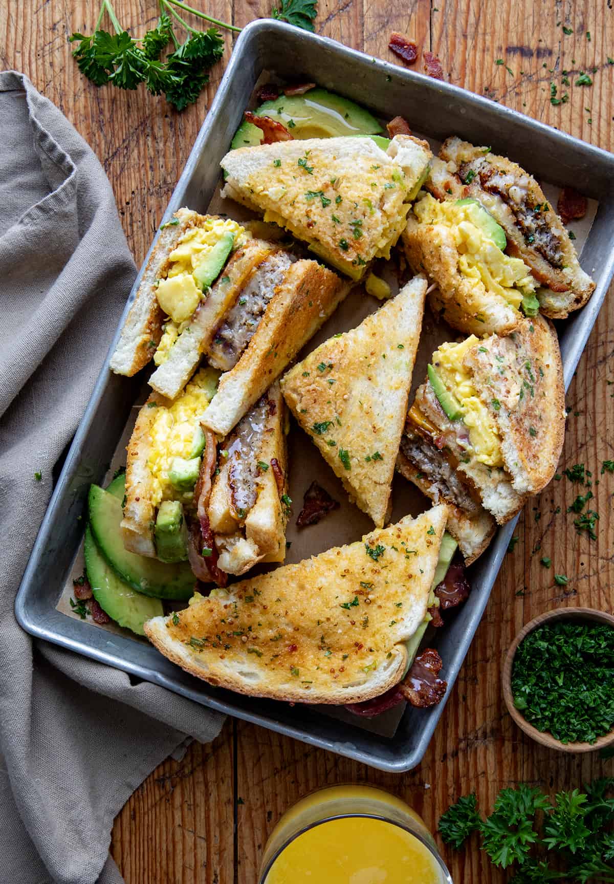 Breakfast Club Sandwiches in a pan on a wooden table with Orange Juice from overhead.