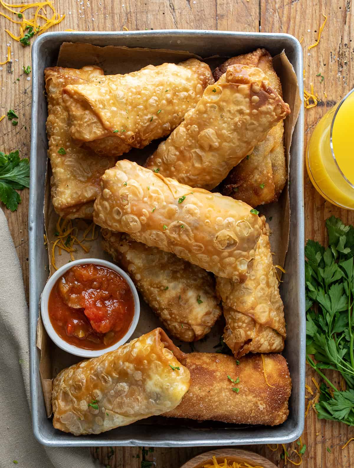 Steak Egg and Cheese Egg Rolls in a Pan with Salsa on a Wooden Table with Orange Juice from Overhead.