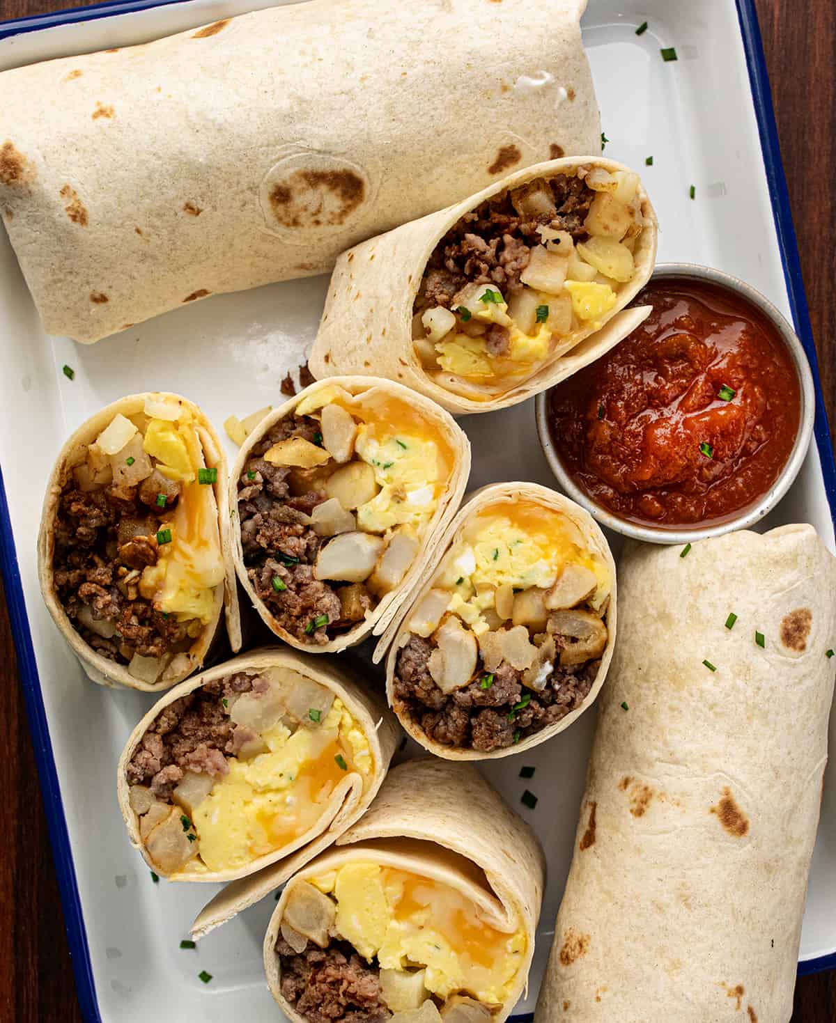 Pan of Breakfast Burritos with Salsa and Sour Cream and Some Burritos Cut in Half Showing Inside Texture. 