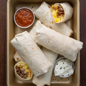 Pan of Breakfast Burritos with Salsa and Sour Cream and one Burrito Cut in Half Showing Inside Texture.