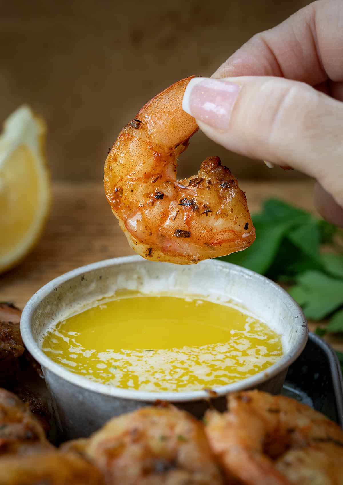 Hand Holding a Piece of Cajun Shrimp Over Butter.