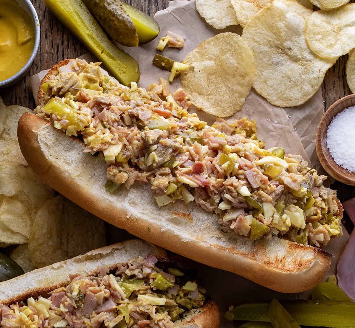 Cuban Chopped Grinder Sandwiches on a Table with Pickles, Chips, More Sandwiches.
