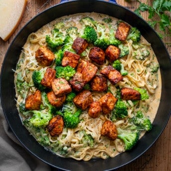 Skillet of Blackened Salmon and Broccoli Alfredo on a Table from Overhead with Parmesan Near.