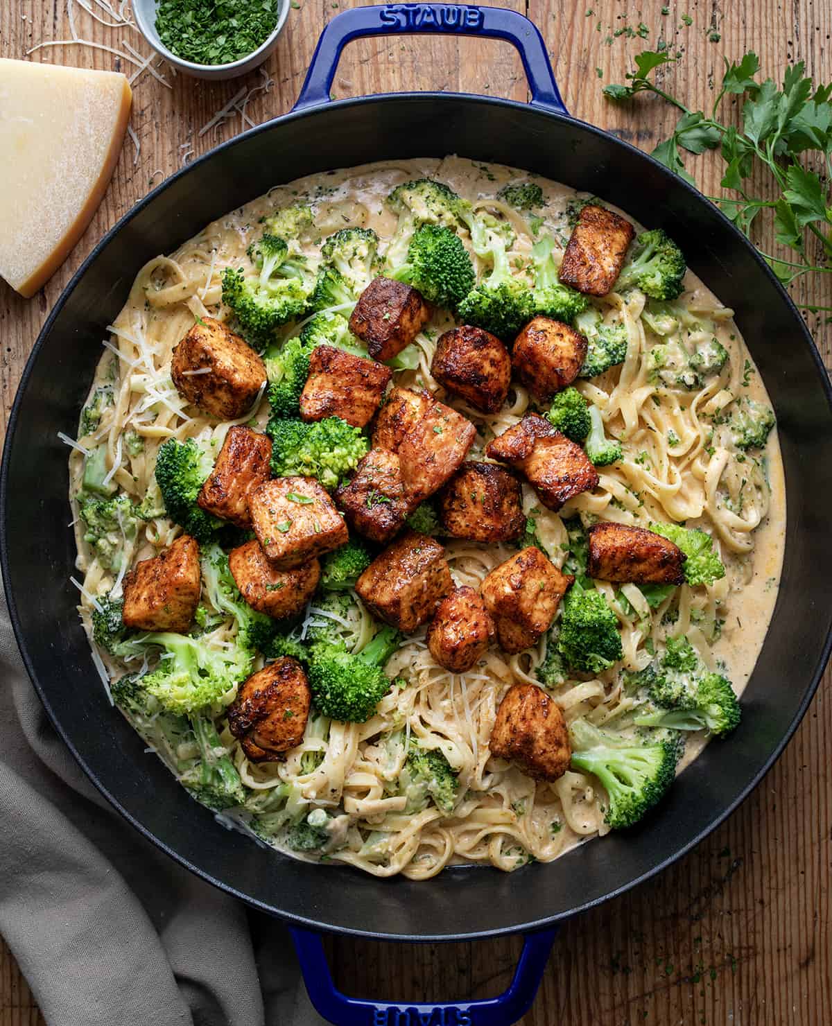 Skillet of Blackened Salmon and Broccoli Alfredo on a Table from Overhead with Parmesan Near.

