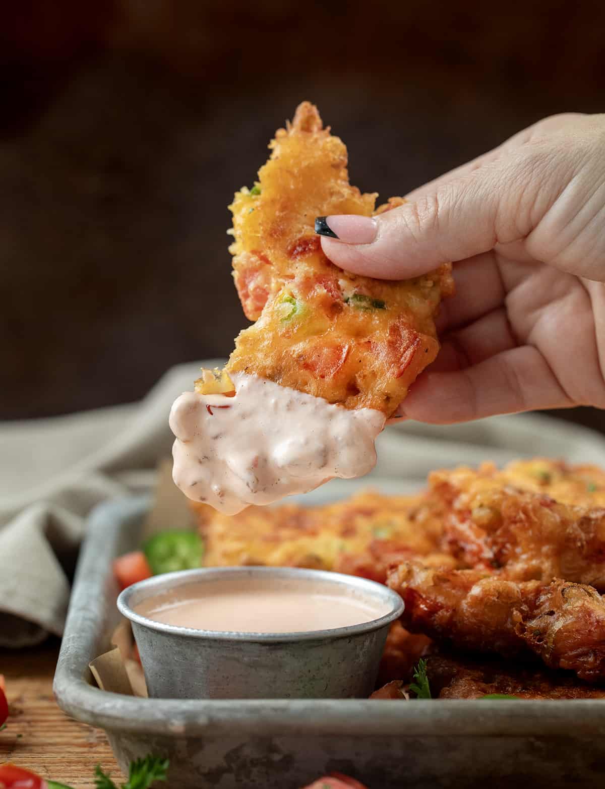 Hand Holding a Cut in Half Tomato Fritter and Dipping it into Tomato Mayo.