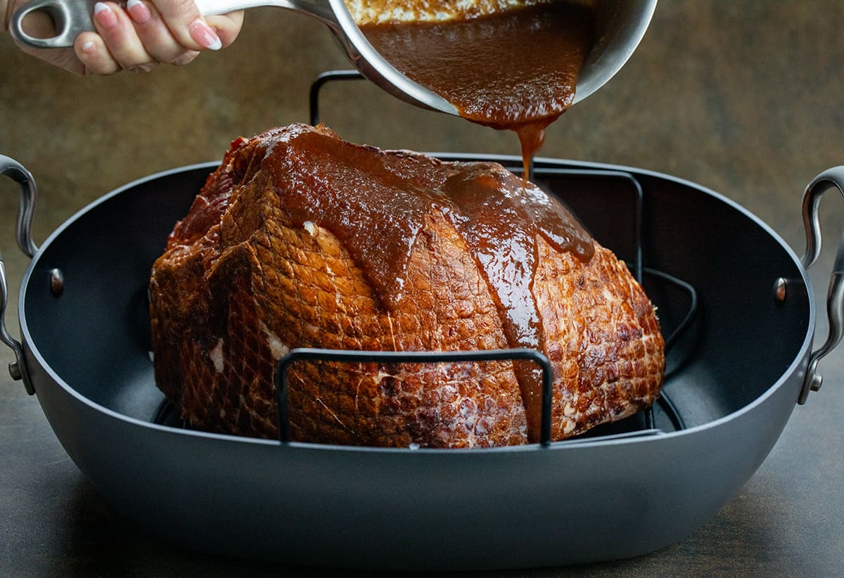 Pouring apple butter glaze over an unbaked ham.