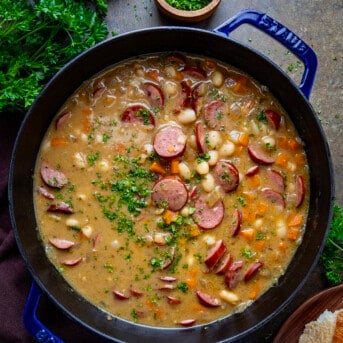 Pot of Creamy Bean Soup With Kielbasa on a Dark Table with Parsly and Bread from Overhead.