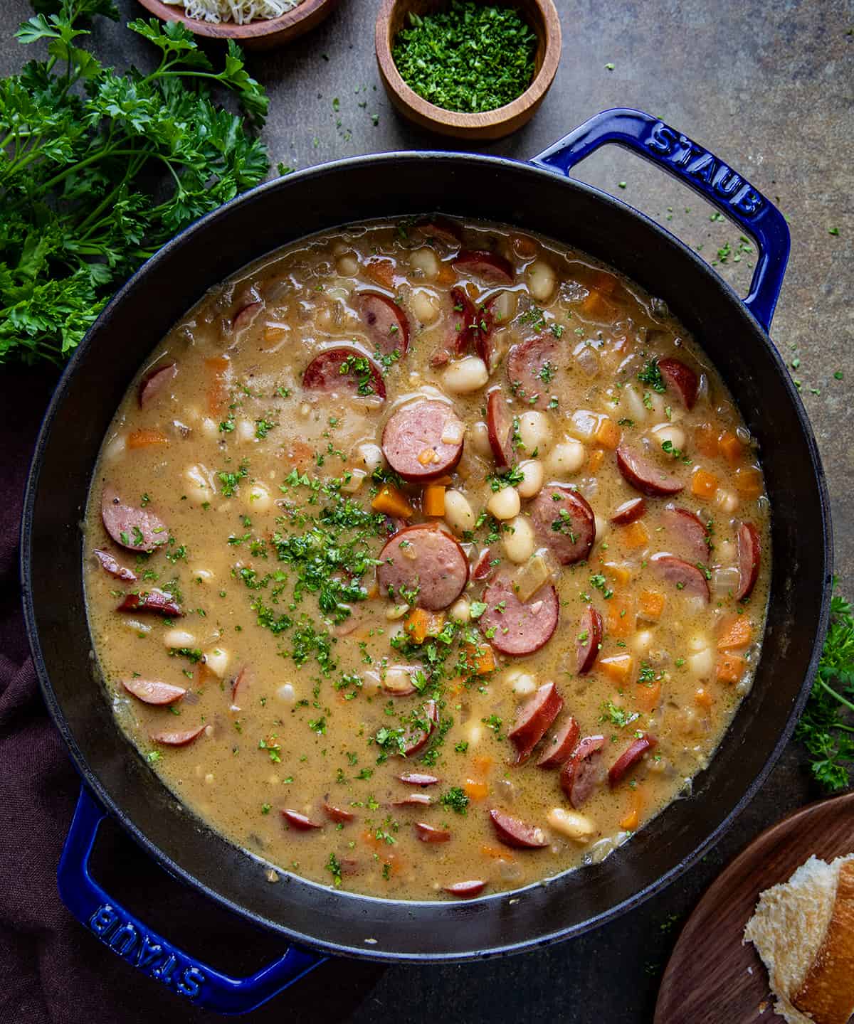 Pot of Creamy Bean Soup With Kielbasa on a Dark Table with Parsly and Bread from Overhead.