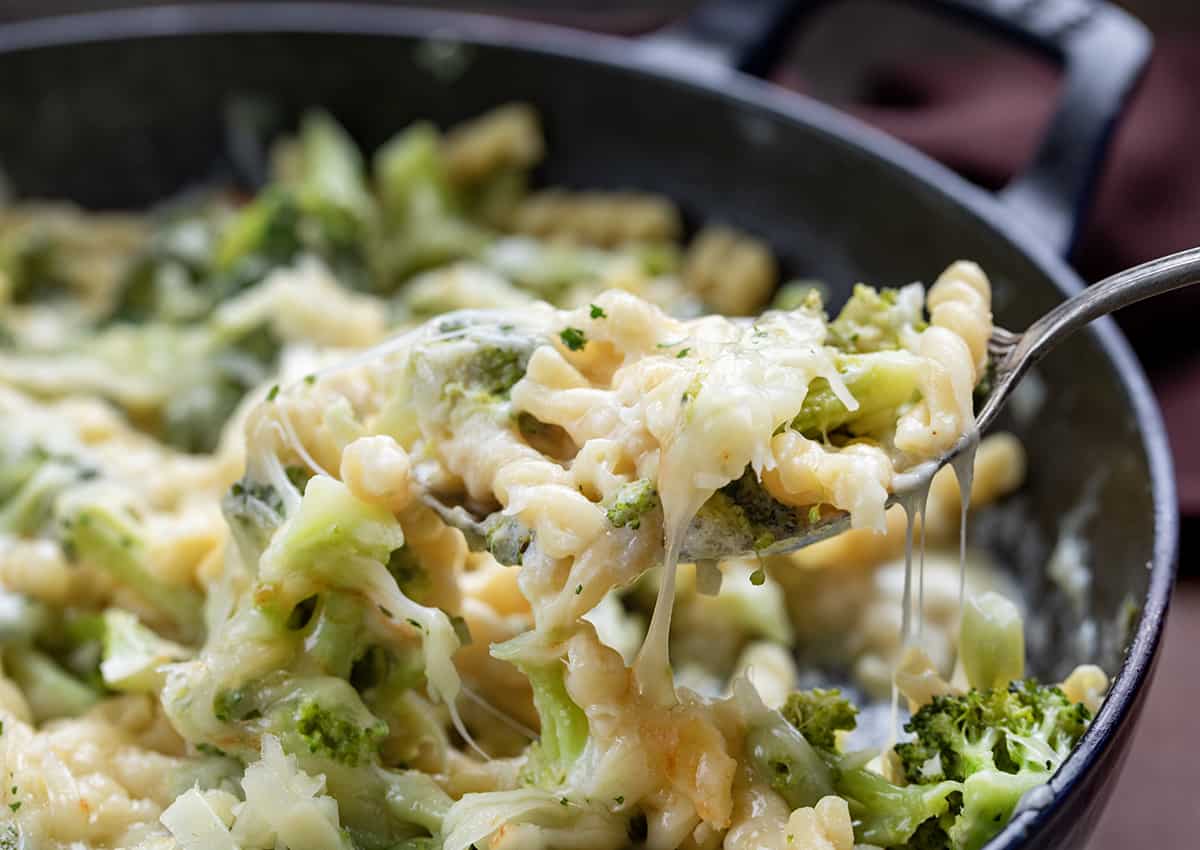 Spoon Scooping Broccoli Cheese Pasta out of a Skillet Up Close.