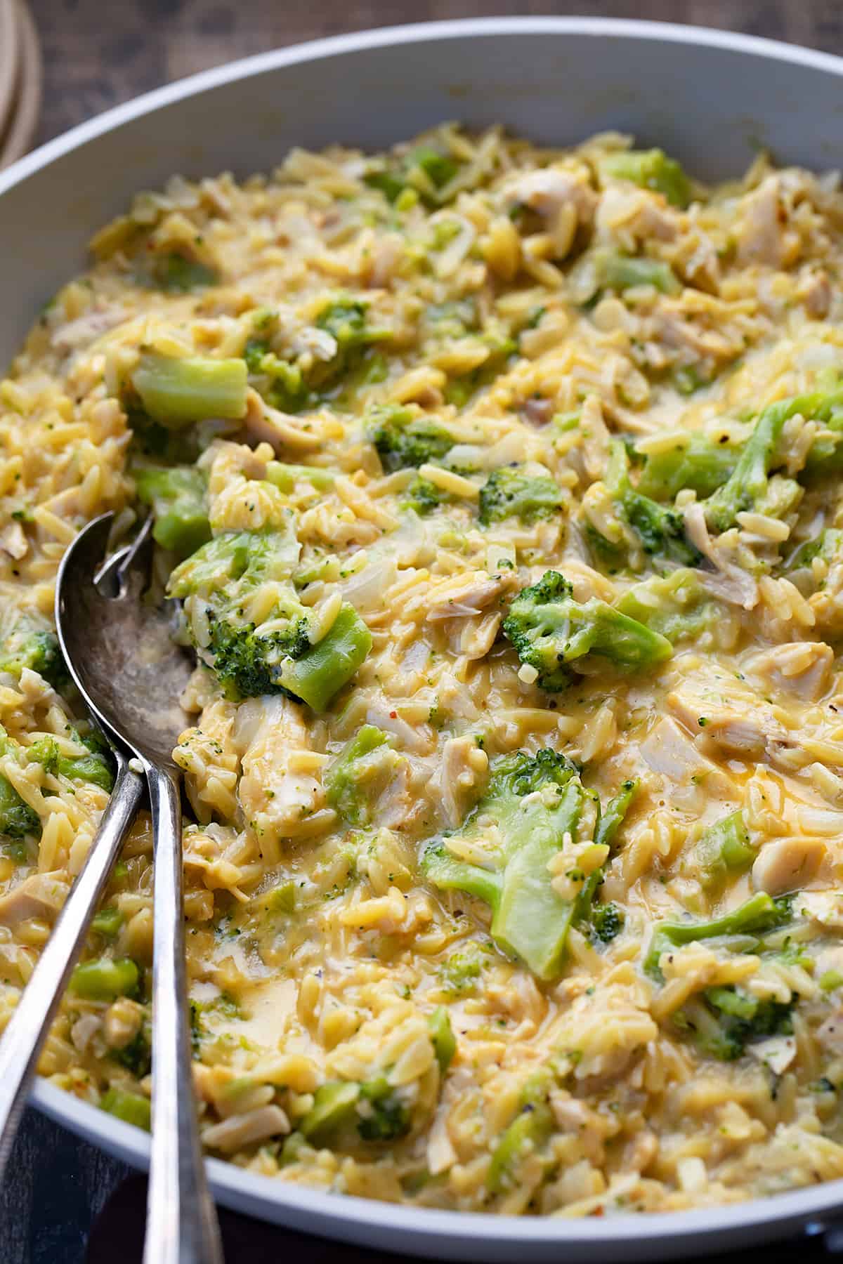 Spoons nestled into Creamy Chicken and Broccoli Orzo in a skillet.