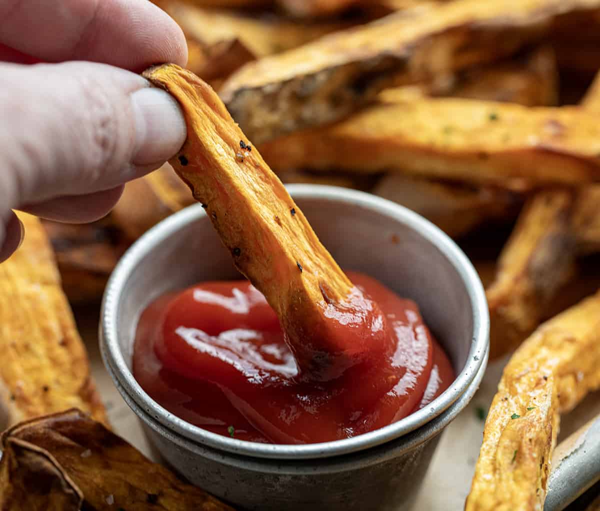 Hand Dipping a Sweet Potato Fry into Ketchup.