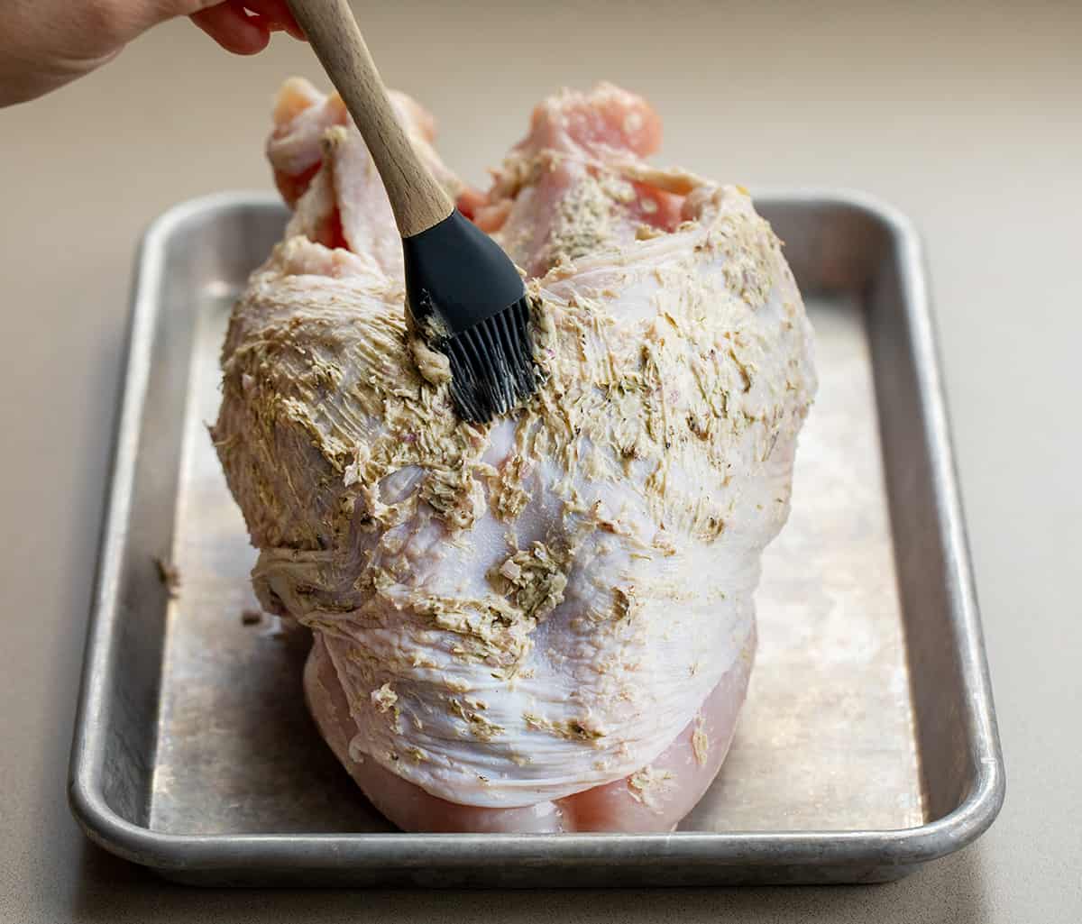 Adding butter and herbs to a raw turkey breast.