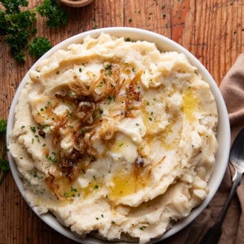 Looking down on a bowl of French Onion Mashed Potatoes on a wooden table.