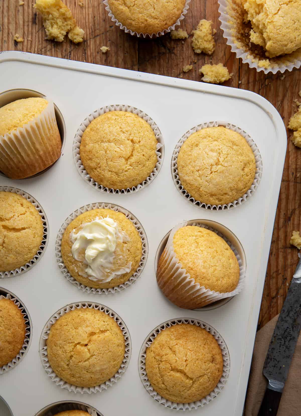 Cornbread Muffins in a muffin tin with some butter on a wooden table.