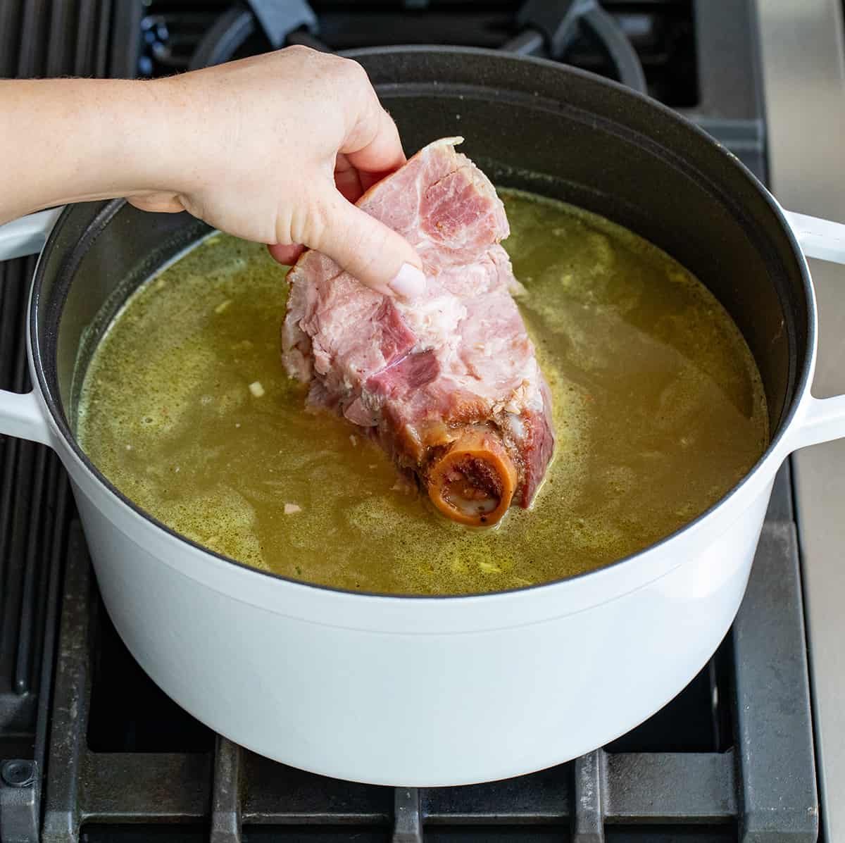 Adding hambone to soup broth in a pot.