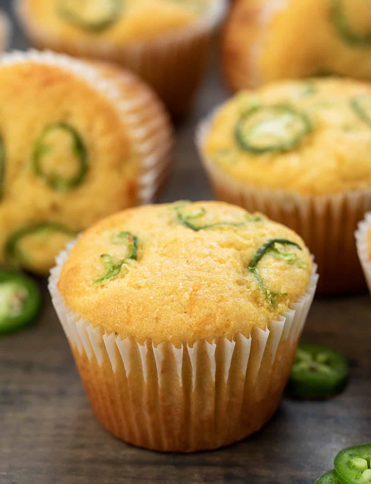 A Jalapeno Cheddar Cornbread Muffin on a wooden table in front of other muffins.
