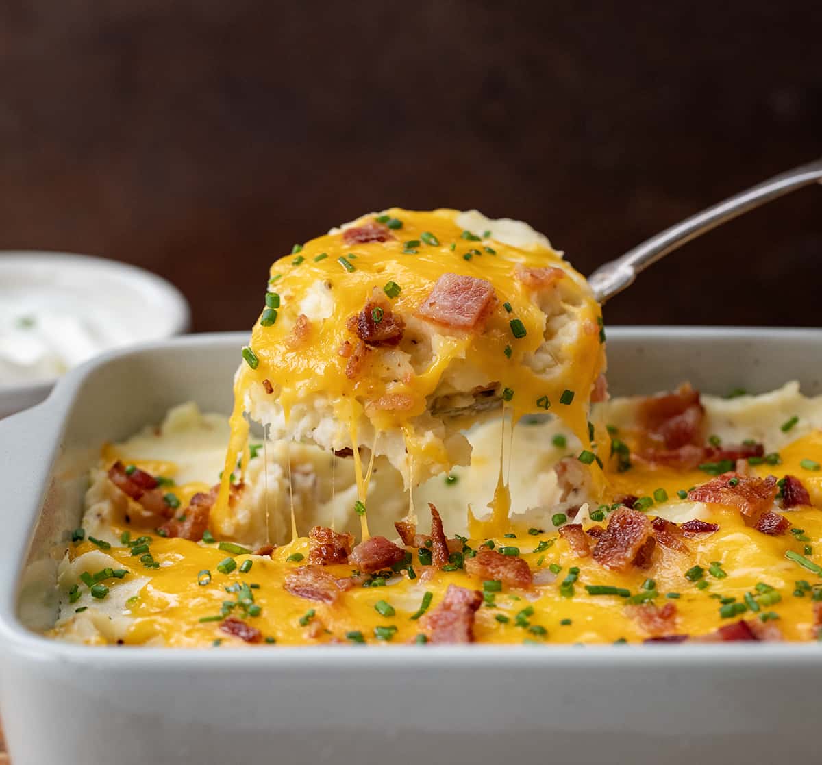 Spoon picking up a portion of Loaded Mashed Potatoes from the pan.