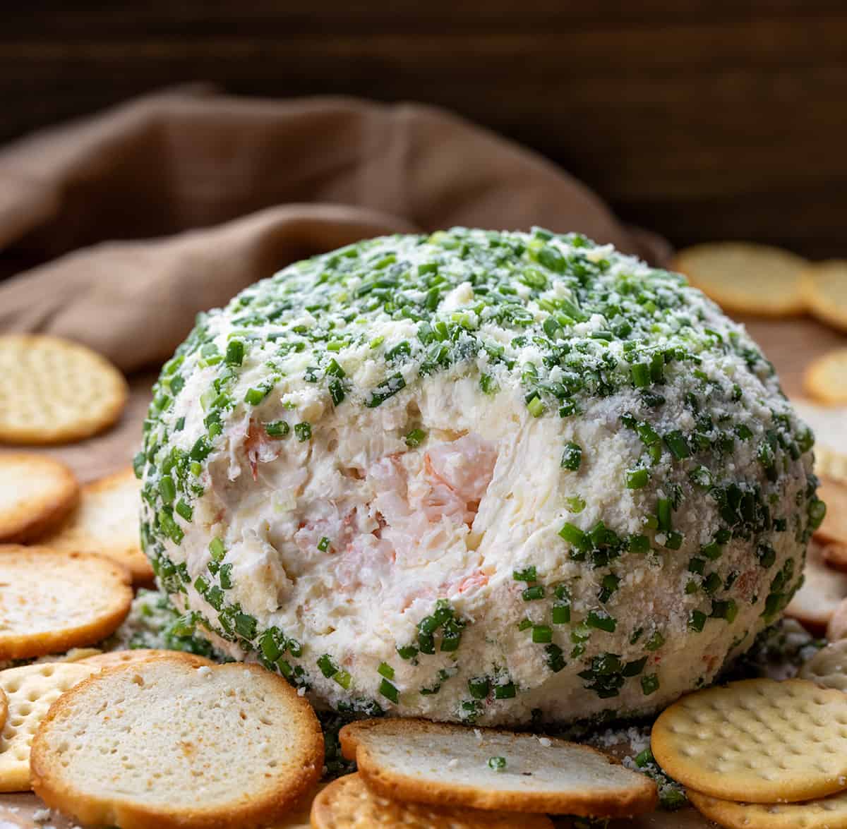 Whole Shrimp Cheese Ball with some of the dip removed showing inside surrounded by crackers. 