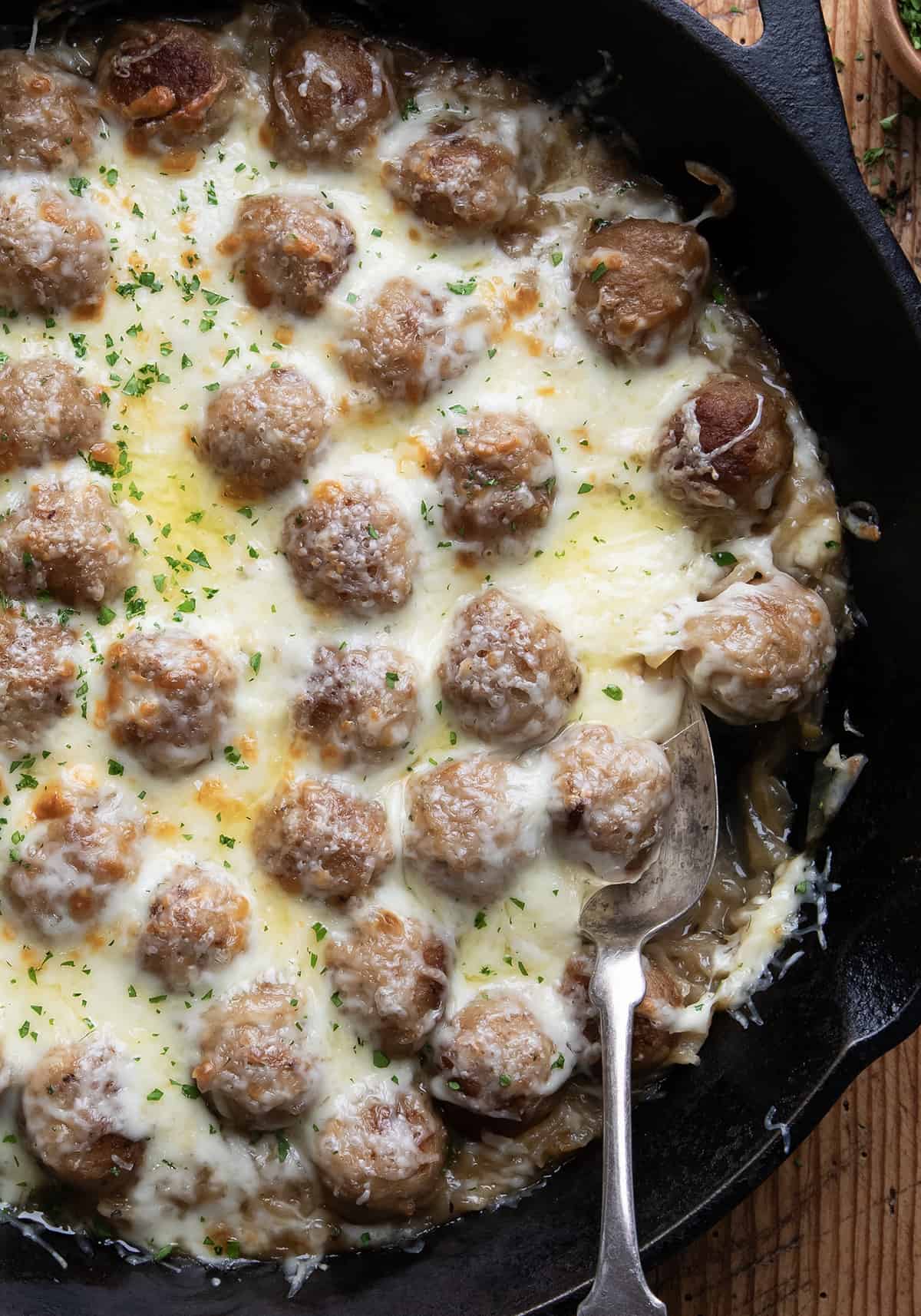 Close up of French Onion Meatballs in a skillet with a spoon.