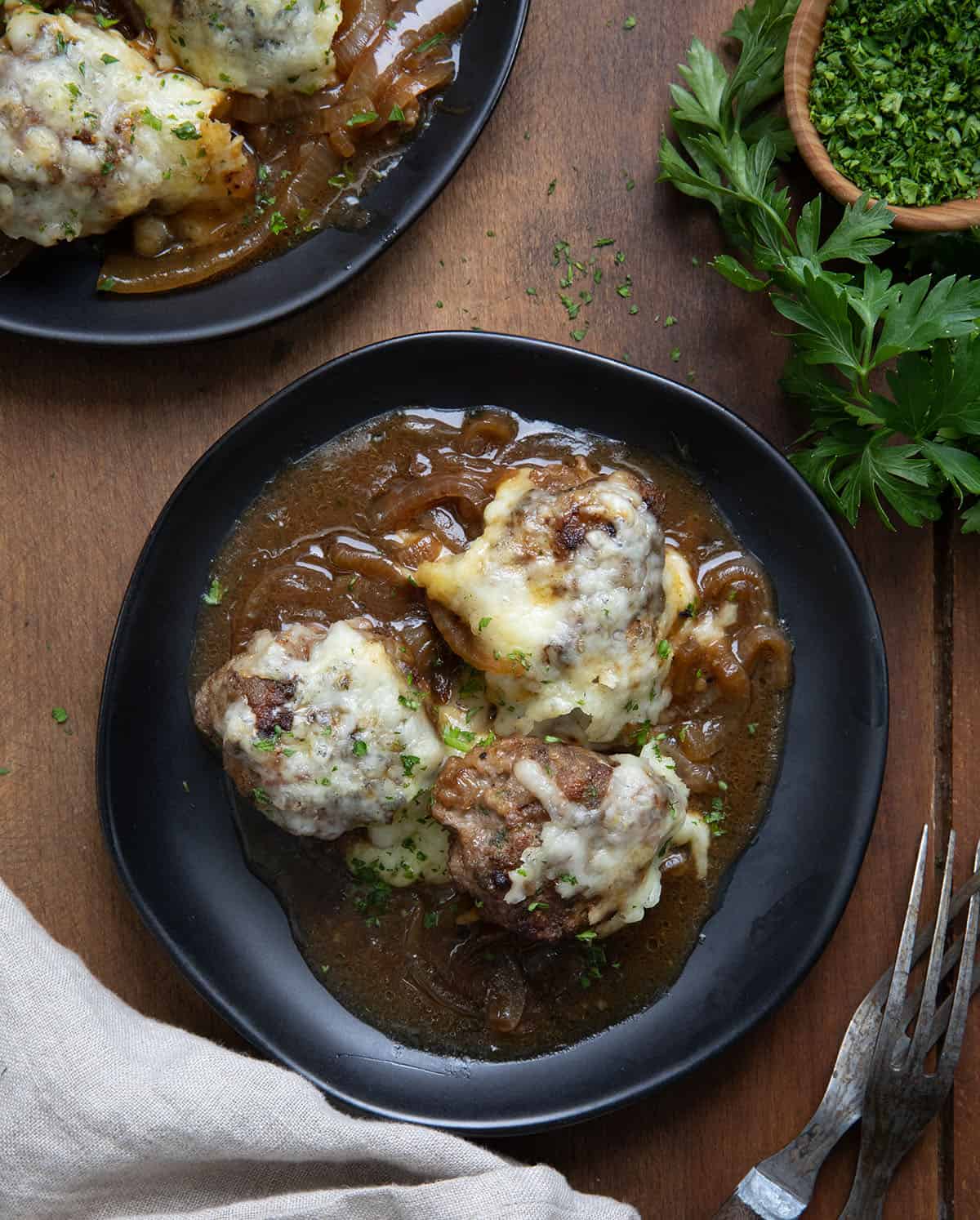 Three French Onion Meatballs on a black plate on a wooden table from overhead.