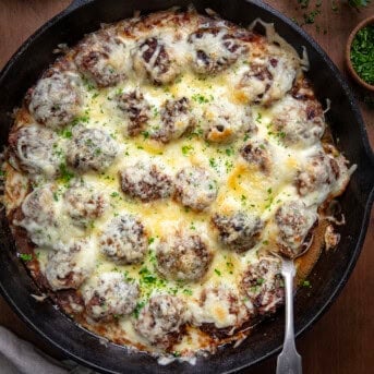 Skillet of French Onion Meatballs with a spoon in the pan on a wooden table from overhead.