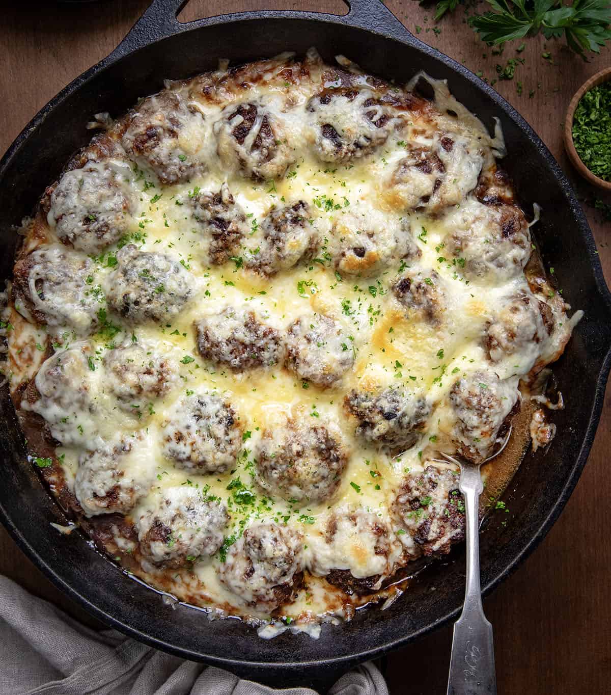 Skillet of French Onion Meatballs with a spoon in the pan on a wooden table from overhead.