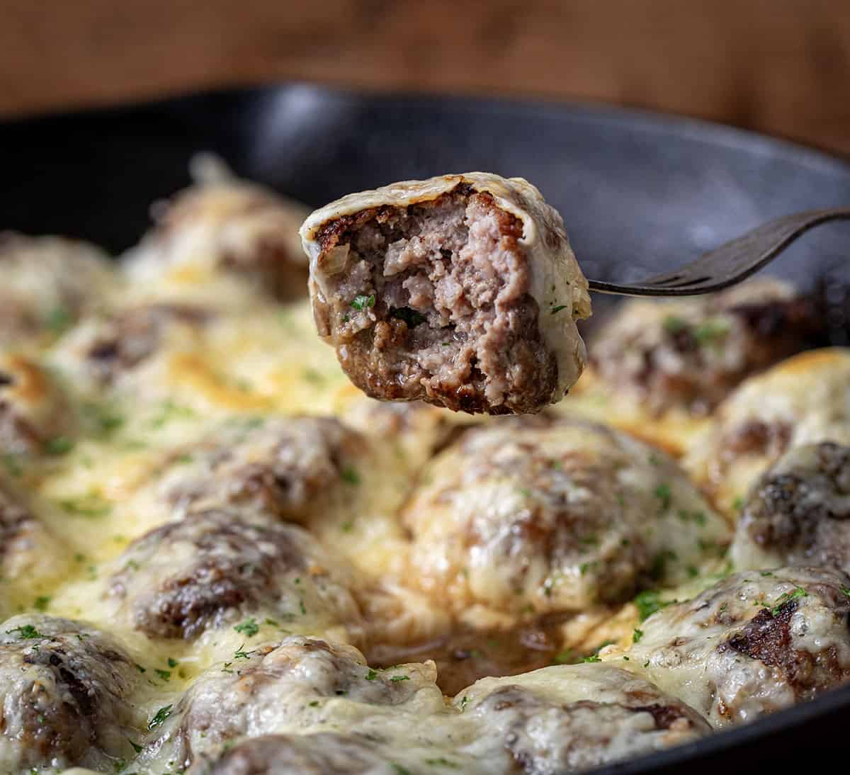 Fork holding a bit into French Onion Meatball over the pan.