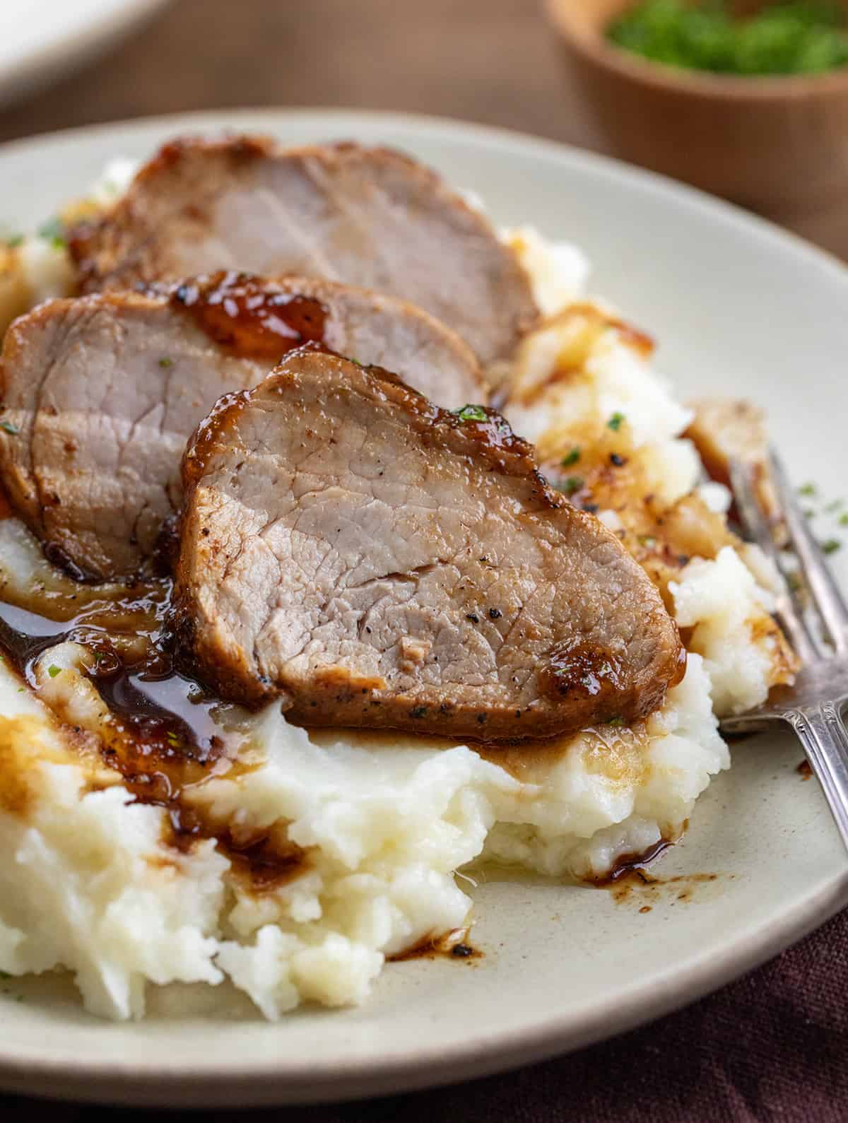 Close up of slices of Pork Tenderloin With Apricot Glaze on mashed potatoes.